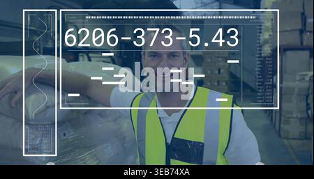 Lavoratore pendente che indossa un giubbotto di sicurezza giallo neon su una polo bianca, sorridendo vicino a pallet avvolti e HUD Foto Stock