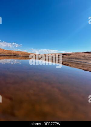 Vista di una pozza d'acqua che riflette il cielo azzurro e le formazioni rocciose rosse del Capitol Reef National Park, Utah, Stati Uniti. Foto Stock