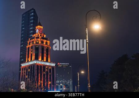 Batumi, georgia 21 aprile 2026: Vista notturna della città di batumi, una torre dell'orologio sheraton illuminata e un edificio alberghiero marriott in piedi sotto un cielo buio, con Foto Stock
