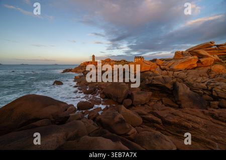 Vista del faro di Ploumanaca'h, situato sulla costa di granito rosa con grandi massi e una casa sotto il cielo del tramonto a Perros-Guirec, Bretagne, F. Foto Stock