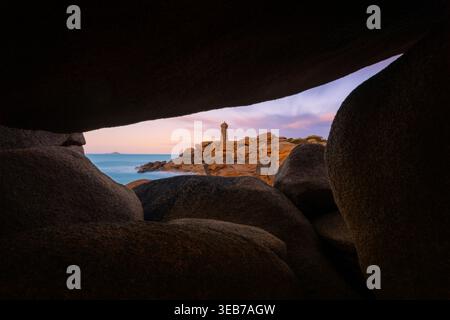 Vista del faro di Ploumanaca'h incorniciato da massicci massi di granito rosa lungo la costa rocciosa sotto un morbido cielo crepuscolo a Perros-Guirec, in Bretagna, Foto Stock