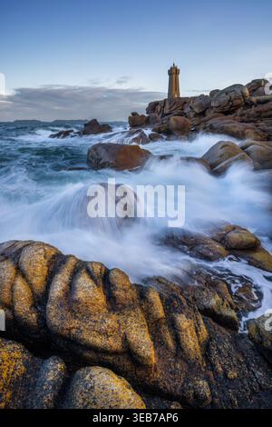 Veduta del faro di Ploumanac'h che si erge su rocce di granito rosa con onde che si infrangono su massi sotto un cielo azzurro limpido Perros-Guirec, Bretagne, p. Foto Stock