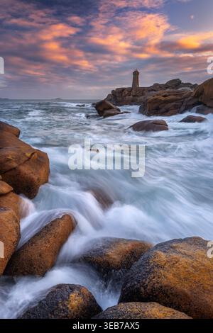 Veduta del faro di Ploumanac'h che sorge su rocce di granito rosa con onde che si infrangono sotto il cielo del tramonto a Perros-Guirec, Bretagna, Francia. Foto Stock
