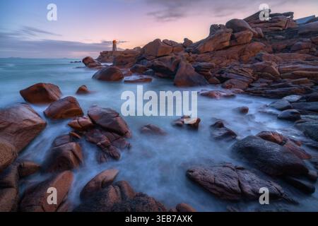 Veduta del faro di Ploumanaca'h che sorge su rocce di granito rosa con acqua di mare nebbiosa al crepuscolo a Perros-Guirec, Bretagne, Francia. Foto Stock