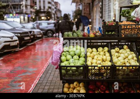 Batumi, georgia, 21 aprile 2026: Bancarello del mercato di batumi Street con casse colorate di mele fresche, arance e avocado in una pista ciclabile rossa e in una traff della città Foto Stock