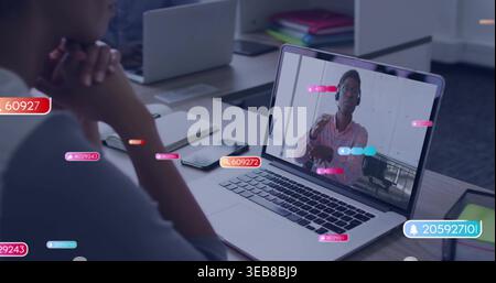 Visualizzazione di un computer portatile aperto con un presentatore che indossa l'auricolare, camicia a motivi geometrici alla scrivania, con sovrapposizioni Foto Stock