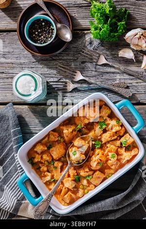 Aloo Gobi Matar con merluzzo, curry di pesce indiano con cavolfiore e piselli verdi in un piatto da forno blu con cucchiaio su un tavolo di legno con spezie, prezzemolo e Foto Stock
