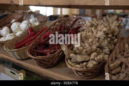 Zenzero fresco, peperoni rossi e aglio esposti in cesti di vimini in un negozio di fattoria. Foto Stock