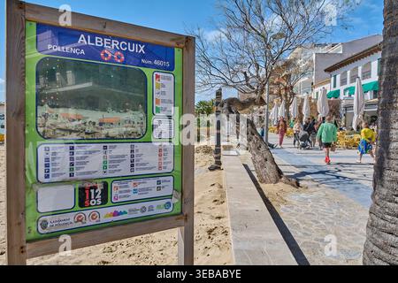Mallorca Spagna - 25 aprile 2026: Un'informativa bacheca di sicurezza si trova all'ingresso della spiaggia di Albercuix a Pollenca, con turisti che passeggiano lungo Foto Stock