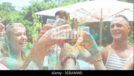 Tostare quattro amici che allevano bottiglie di birra e bicchieri nel patio del cortile, con coriandoli colorati Foto Stock