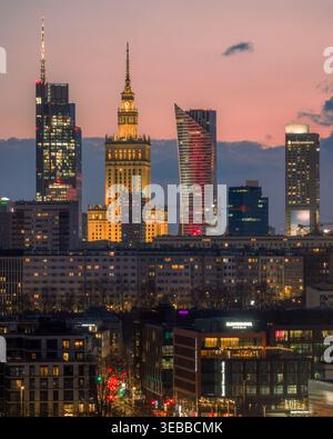 Varsavia, Polonia - 20 marzo 2026: Vista aerea del Palazzo della Cultura e della Scienza e dei moderni grattacieli sotto un cielo rosa al tramonto. Foto Stock