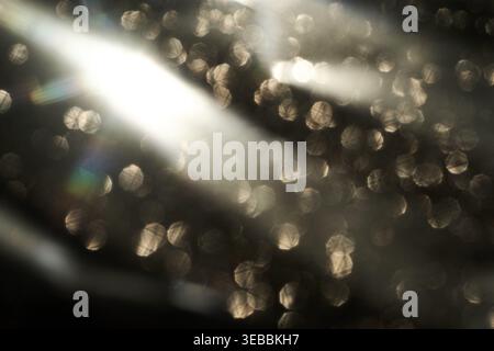 Bokeh con luce d'argento sulla superficie sfocata scura con striature e riflessi nelle impostazioni ambiente basso messa a fuoco morbida e toni neutri. Foto Stock