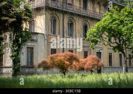 Vista esterna di una vecchia villa storica con facciata testurizzata e alberi di colore autunnale, catturata alla mostra Alcova durante la Milano Design Week Foto Stock