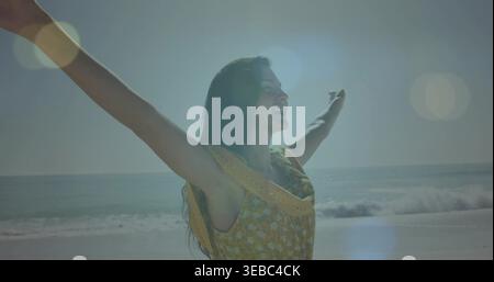 Braccia strette, donna con abito floreale senza maniche giallo che guarda al sole sulla spiaggia sabbiosa, lucentezza Foto Stock