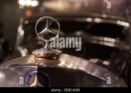 Fotografia ravvicinata di un emblema vintage a tre punte Mercedes-Benz montato su una superficie cromata lucida. L'iconico emblema argentato Foto Stock