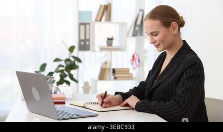Insegnante di inglese che dà lezioni online tramite computer portatile alla scrivania bianca in classe Foto Stock