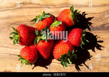 Fragole fresche, inglesi, di nuova stagione disposte su una tavola rustica in legno con luce naturale Foto Stock