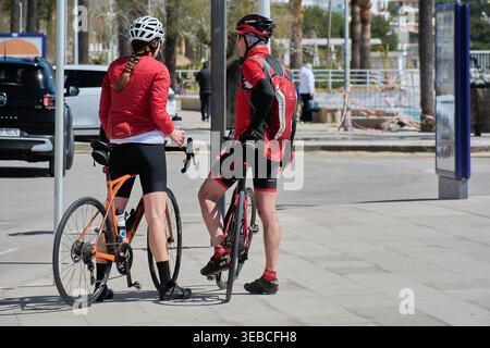 Maiorca Spagna - 25 aprile 2026: Due ciclisti con attrezzatura professionale rossa e nera si fermano su una passeggiata costiera soleggiata durante una corsa in bici primaverile Foto Stock