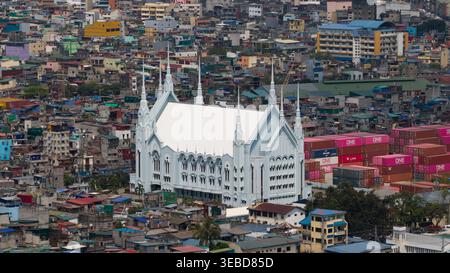 Manila, Filippine - 1 marzo 2026: Veduta aerea di una grande chiesa bianca con più guglie circondata da densa abitazioni urbane e container di spedizione Foto Stock