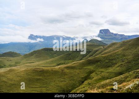 Cima innevata su vasti campi lussureggianti con nuvole nebbiose Foto Stock