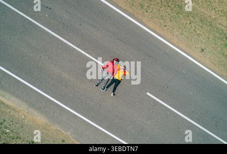 Vista aerea di una coppia di viaggiatori riposano su una strada vuota rettilinea, godendo di tranquillità con le mani dietro la testa Foto Stock
