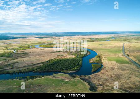 La vista panoramica di un tortuoso fiume scorre attraverso vaste praterie e foreste sotto un cielo primaverile limpido Foto Stock