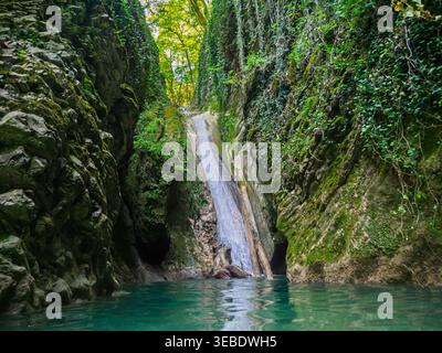 Splendida cascata che si tuffa in una limpida piscina turchese immersa in un vivace canyon verde e muscoloso Foto Stock