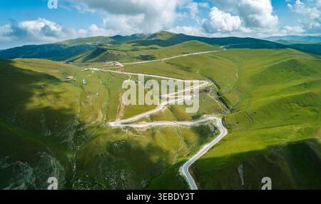 Vista panoramica della tortuosa strada di montagna che attraversa lussureggianti pendii verdi sotto un cielo luminoso Foto Stock