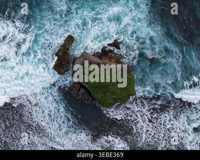 Veduta aerea di un piccolo isolotto roccioso coperto da una lussureggiante vegetazione circondata da potenti onde bianche e profonde acque blu dell'oceano al Baron Bea Foto Stock