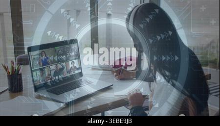 Scrivere un adolescente che indossa un auricolare e prende appunti alla scrivania vicino a una finestra, con un computer portatile e un notebook Foto Stock