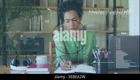 Donna matura che indossa una camicetta verde seduta alla scrivania dell'ufficio, con notebook e penna aperti Foto Stock
