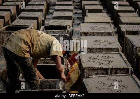 Un ragazzo di 11 anni esegue un pesante lavoro manuale in una fabbrica di cemento in Bangladesh, evidenziando la realtà del lavoro minorile e della povertà. Foto Stock