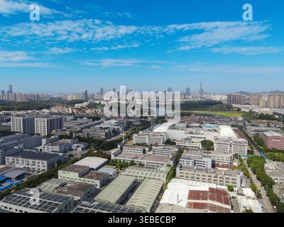 Vista aerea di complessi industriali e magazzini vicino a un fiume tortuoso con un lontano skyline della città sotto un cielo blu Dongguan, provincia del Guangdong, chi Foto Stock