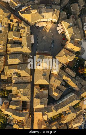 Vista aerea della circolare Piazza del comune circondata da edifici storici in pietra e tetti piastrellati durante l'ora d'oro a Montefalco, Umbria, Ital Foto Stock