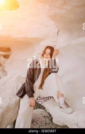 Donna seduta sulle scogliere il giovane viaggiatore in giacca di pelle si rilassa sulle formazioni di roccia bianca durante la luce dorata dell'ora Foto Stock