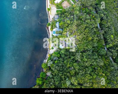 Vista aerea della lussureggiante costa tropicale di Guanaja, caratterizzata da ville di lusso con piscine annidate tra fitti alberi verdi e acque turchesi Foto Stock