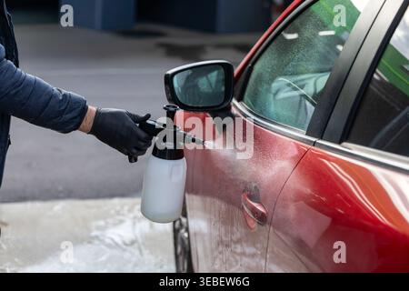 Applicazione del detergente in schiuma sulla portiera rossa dell'auto durante il processo di lavaggio self-service professionale Foto Stock