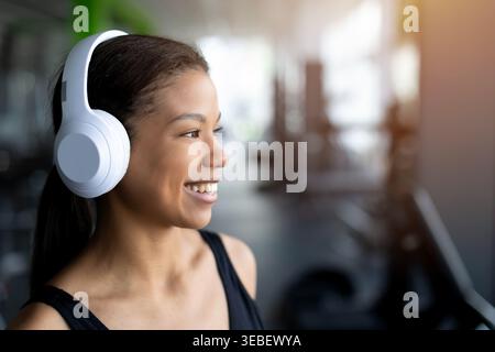 Ritratto di una giovane donna nera sorridente in palestra che indossa cuffie wireless bianche Foto Stock