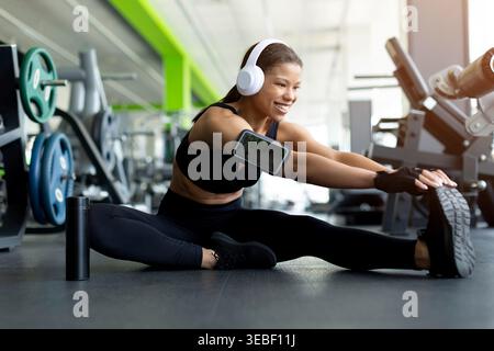 Felice giovane donna nera che fa un distacco laterale seduto sul pavimento della palestra Foto Stock