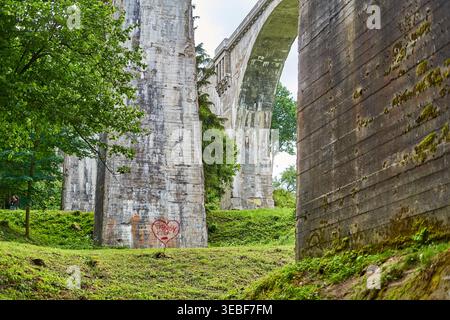 Una vista prospettica a basso angolo di massicci pilastri e archi in cemento eroso appartenenti a una grande struttura di viadotto. Le superfici in cemento Foto Stock