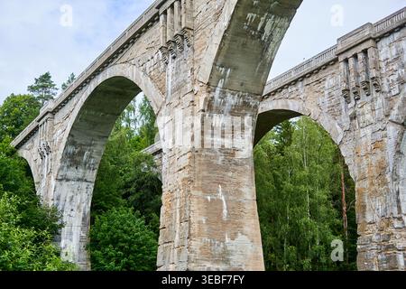 Vista ad angolo basso di un enorme viadotto ferroviario in pietra o cemento eroso, con più grandi archi, che mostra un'età significativa e una superficie consumata Foto Stock