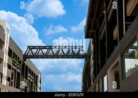 Un ponte a capriata in metallo nero funge da collegamento tra due edifici moderni scuri sullo sfondo di un cielo blu nuvoloso. Foto Stock