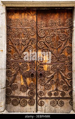 Doppia porta in legno invecchiato con scrolatura in ferro battuto ornato, struttura rustica, telaio in pietra, dettagli architettonici vintage. Foto Stock
