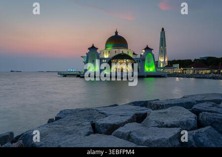 Famosa moschea galleggiante dello stretto di Malacca illuminata durante un tramonto colorato, vista dalla costa rocciosa di Malacca, Malesia Foto Stock