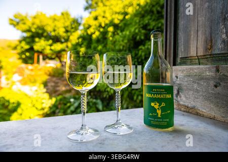 Perdiki, Grecia - 21 giugno 2023: Retsina malamatina vino bianco greco secco con resina di pino in bottiglia di vetro e due bicchieri sull'isola di Ikaria, Grecia Foto Stock