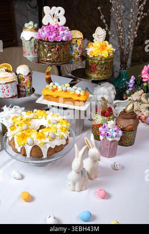 Shot verticale di torte di Pasqua ornate e coniglietti di ceramica su un tavolo bianco. Foto Stock