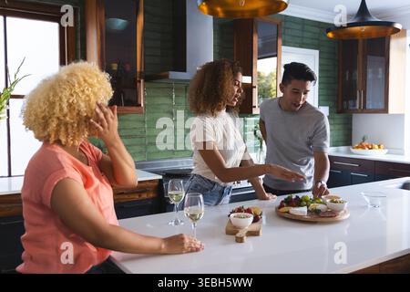 Diversi amici si riuniscono a Kitchen Island, scegliendo tra tagliere rotonde di salumi in legno Foto Stock