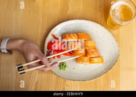Sushi roll al salmone con birra. Vista dall'alto di sushi al salmone con bacchette, zenzero sottaceto, wasabi e un bicchiere di birra su un tavolo di legno. Foto Stock