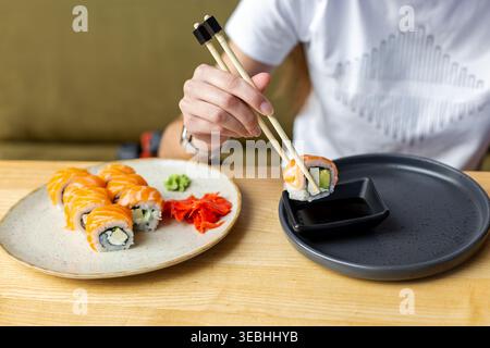 Mangiare sushi di salmone con bacchette. Primo piano di sushi roll di salmone tenuto con bacchette vicino alla salsa di soia, con zenzero e wasabi sul tavolo del ristorante. Foto Stock