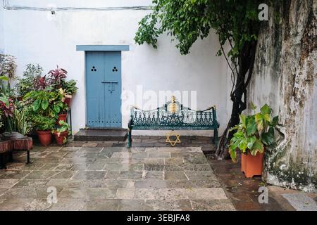 Panca in ghisa ornata con Stella di David su pavimento in pietra nel cortile della sinagoga Pardesi, porta blu Foto Stock